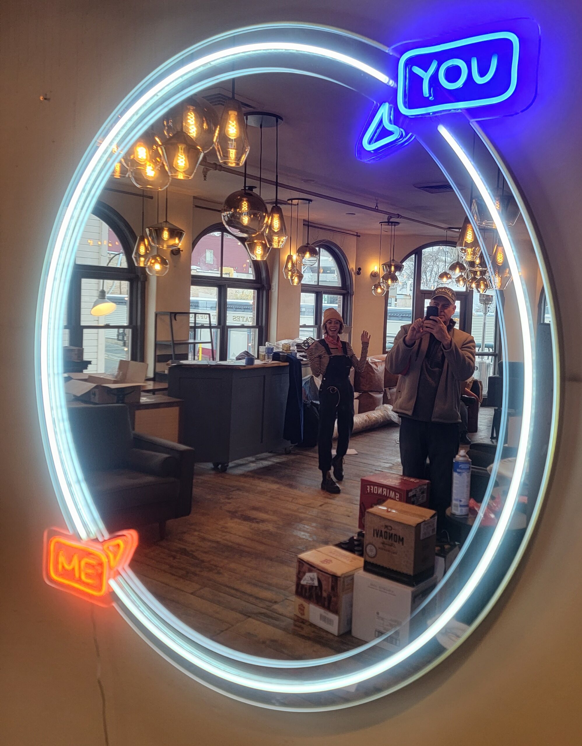 A mirror surrounded by faux-neon LED lights, a white border with a blue arrow saying "You" near the top and an orange arrow saying "Me" near the bottom.